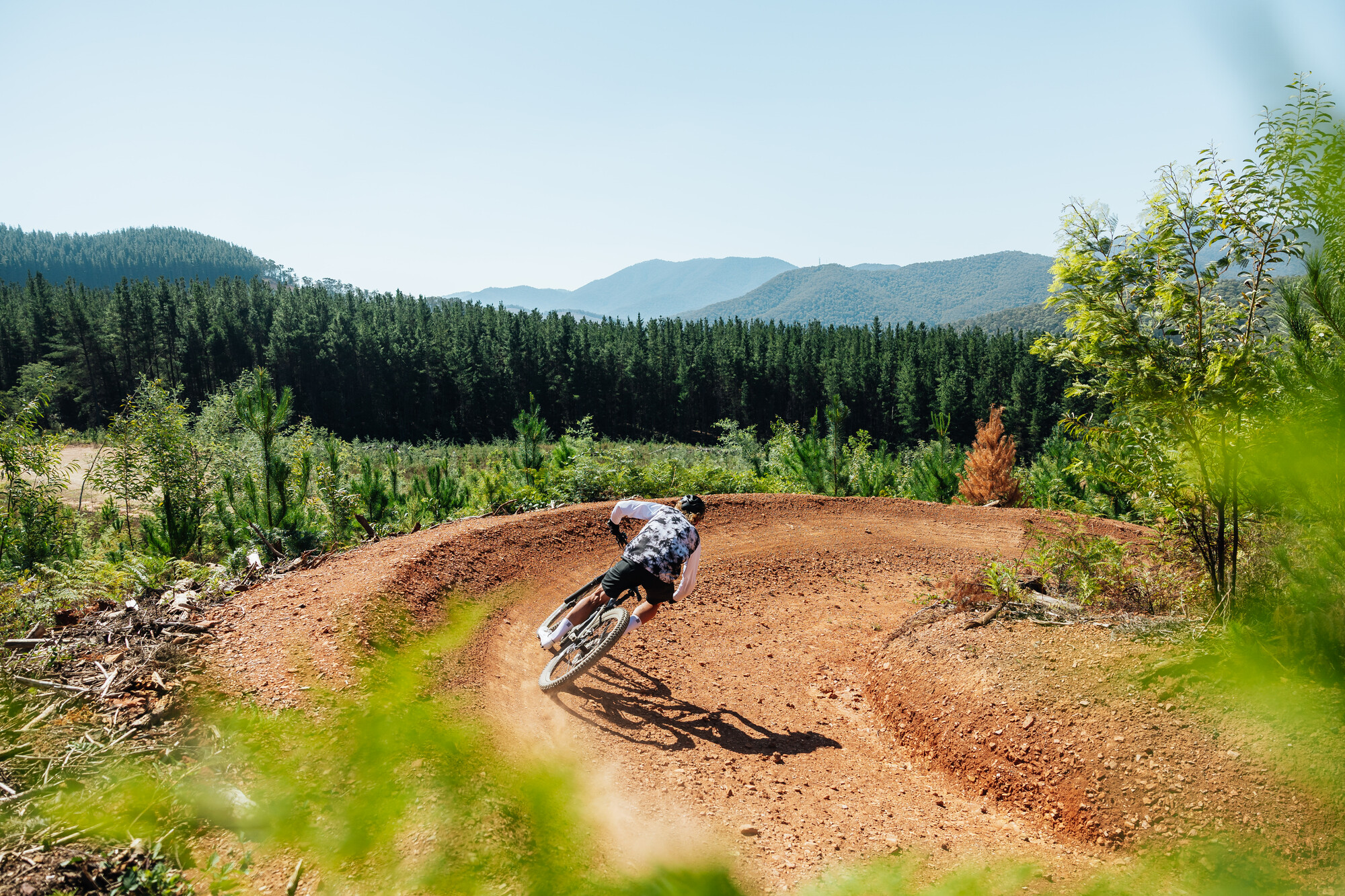 Cyclist riding around a berm at Mystic Bike Park with views of mountains